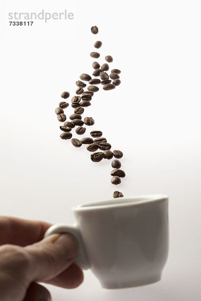 Ein Mann hält eine Kaffeetasse mit darüber schwebenden Kaffeebohnen.