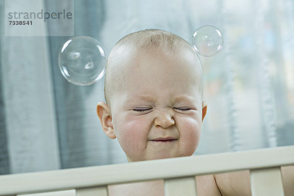 Baby drückt die Augen zu  wenn Blasen an seinem Kopf vorbeiziehen.