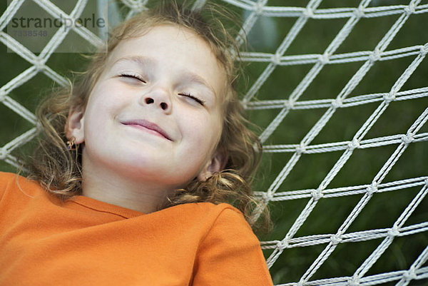 Ein junges lächelndes Mädchen  das mit geschlossenen Augen auf einer Hängematte liegt.