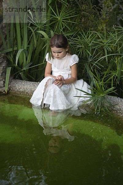 Ein junges Mädchen schaut neugierig ins Teichwasser.