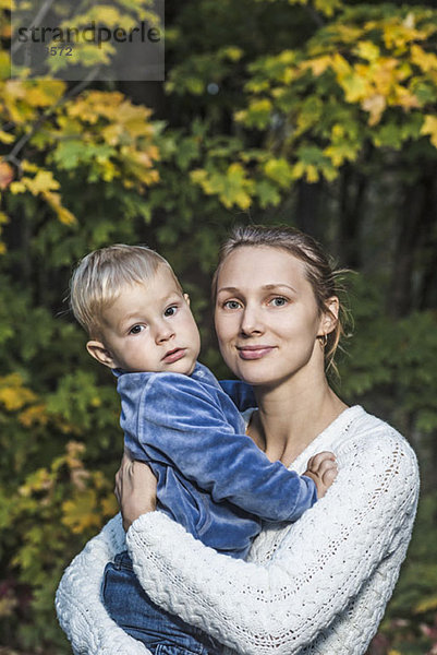 Eine junge Mutter hält ihren Sohn im Herbst in der Hand