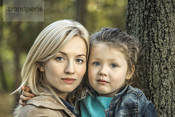 Eine heiter aussehende Mutter und ihre kleine Tochter neben einem Baumstamm