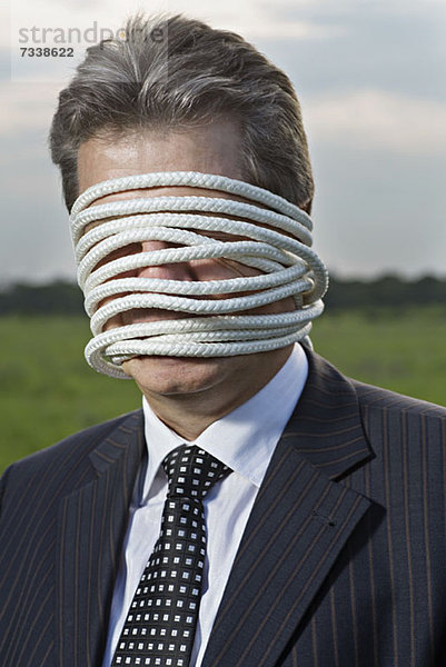 Ein reifer Geschäftsmann mit einem Seil um sein Gesicht gewickelt.