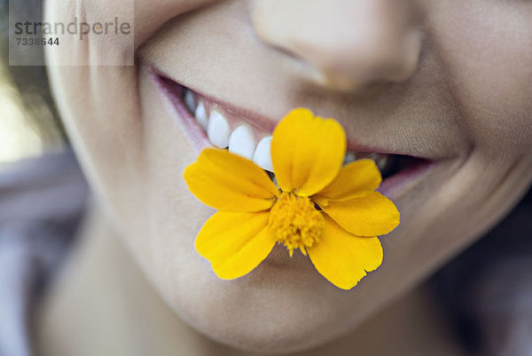 Eine junge grinsende Frau  die eine einzelne Blume in ihrem Mund hält.