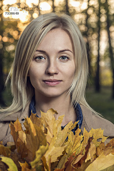 Eine junge Frau hält einen Haufen Herbstblätter in der Natur.