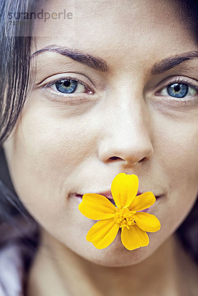 Eine junge Frau  die eine gelbe Blume in ihrem Mund hält.