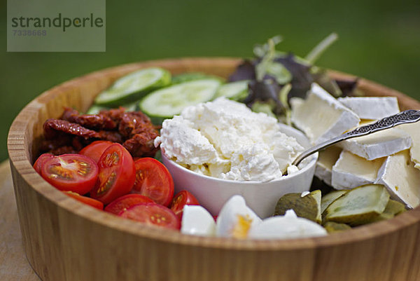 Eine hölzerne Salatschüssel gefüllt mit verschiedenen Gemüsen und Käsesorten.