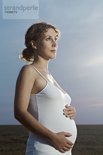 Eine schwangere Frau hält ihren Bauch und schaut nachdenklich weg.