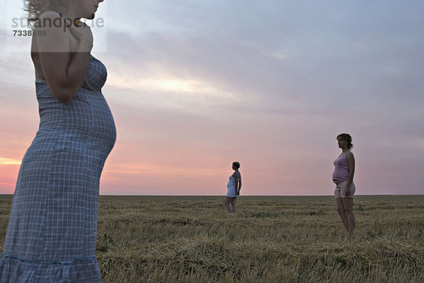 Ein zusammengesetztes Bild von drei Versionen derselben schwangeren Frau auf einem Feld.