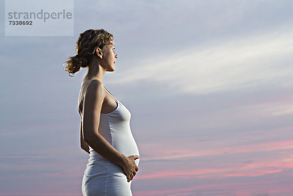 Eine schwangere Frau hält ihren Bauch und schaut in einen dramatischen Himmel.