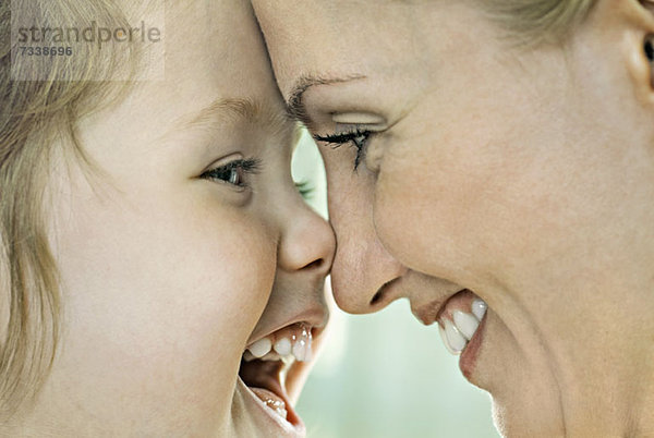 Ein lachendes Mädchen  das mit seiner lächelnden Mutter die Nase berührt  Nahaufnahme