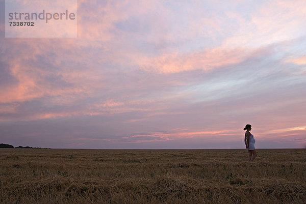 Eine schwangere Frau steht in einem abgelegenen Feld unter einem dramatischen Himmel.