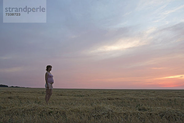 Eine schwangere Frau steht in einem abgelegenen Feld unter einem dramatischen Himmel.