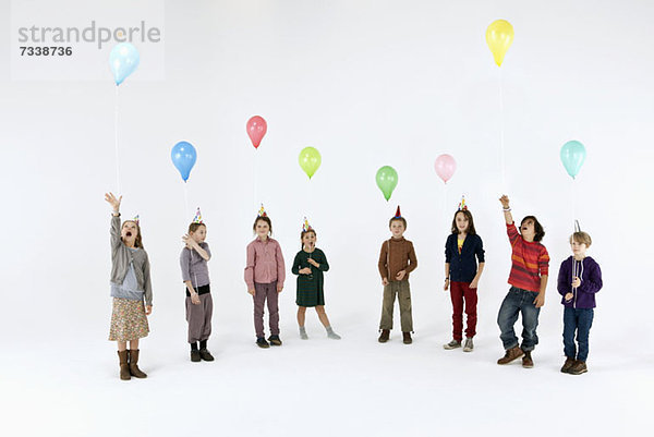 Eine Gruppe von meist gelangweilt aussehenden Kindern mit Ballons und Partyhüten