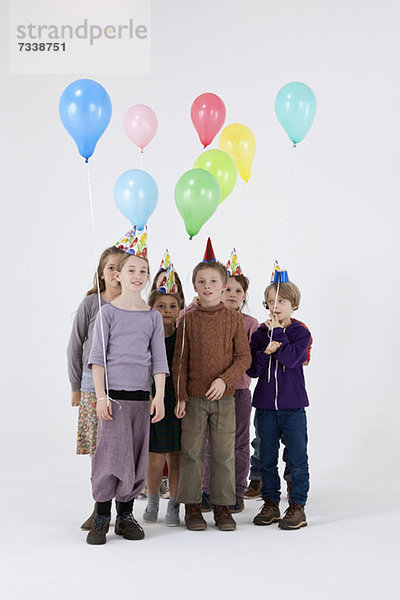 Eine Gruppe von Kindern trägt Partyhüte und hält Luftballons.