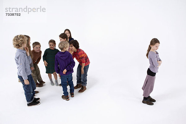Ein Mädchen  das allein steht  die Arme verschränkt  während eine Gruppe von Kindern über sie klatscht.