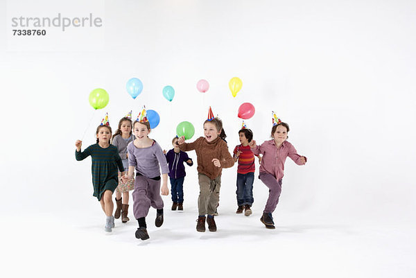 Eine Gruppe von Kindern mit Partyhüten und Luftballons  die vorwärts rennen.