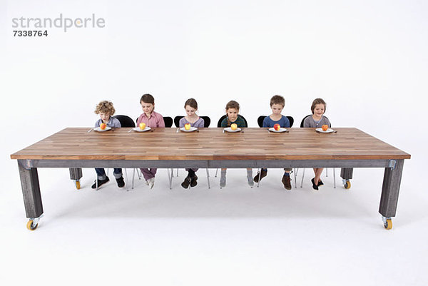 Sechs Kinder schauen unsicher auf die Äpfel auf dem Teller.