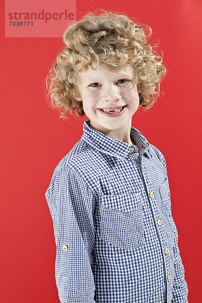 Ein Junge mit strubbeligen  lockigen  blonden Haaren  der die Kamera anlächelt.