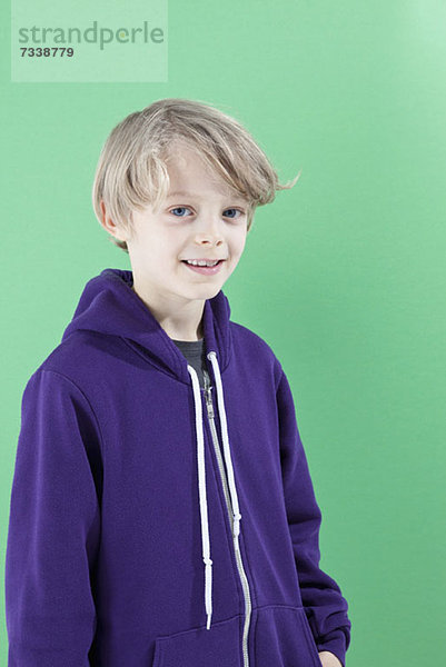 Ein Junge in einem lila Kapuzensweatshirt lächelt in die Kamera.