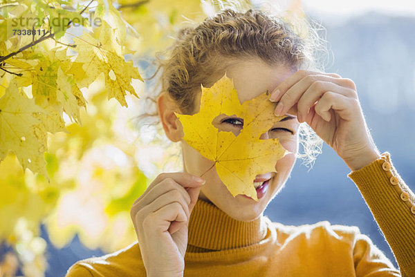 Eine Frau  die durch ein Loch in einem Blatt schaut  das sie an ihr Gesicht hält.