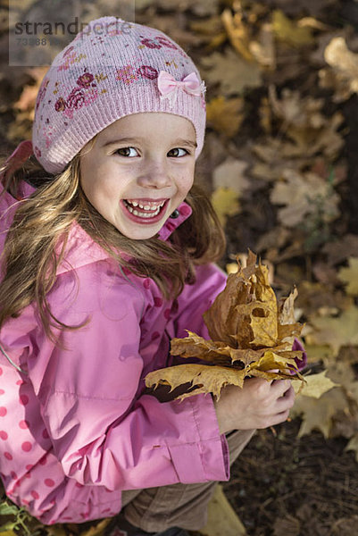 Ein junges Mädchen hält einen Haufen Herbstblätter in der Hand.