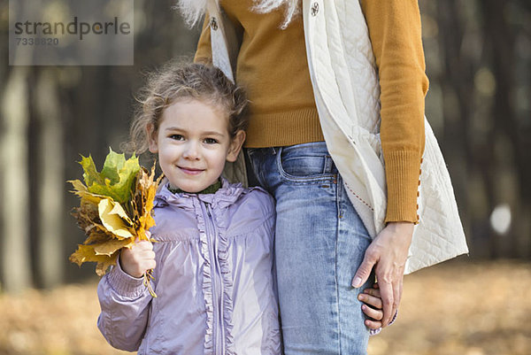 Ein junges Mädchen hält einen Blumenstrauß aus Herbstblättern und hält ihre Mutter fest.