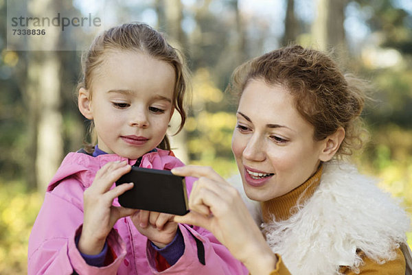 Eine kleine Tochter  die ihrer Mutter etwas auf einem Smartphone zeigt.