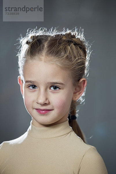 Ein ruhiges junges Mädchen mit einer modischen geflochtenen Frisur und Ohrringen.