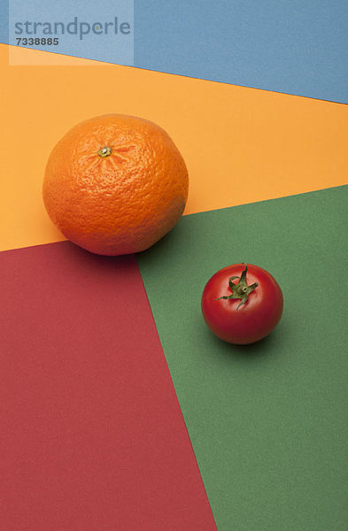 Eine Orange und eine Tomate auf einem mehrfarbigen  geometrischen Muster.