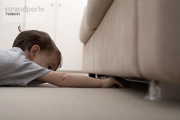 Ein Junge  der unter ein Sofa greift  um etwas zu holen.