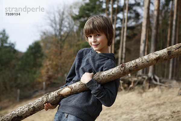 Ein Junge mit einem großen Ast in einem Waldgebiet