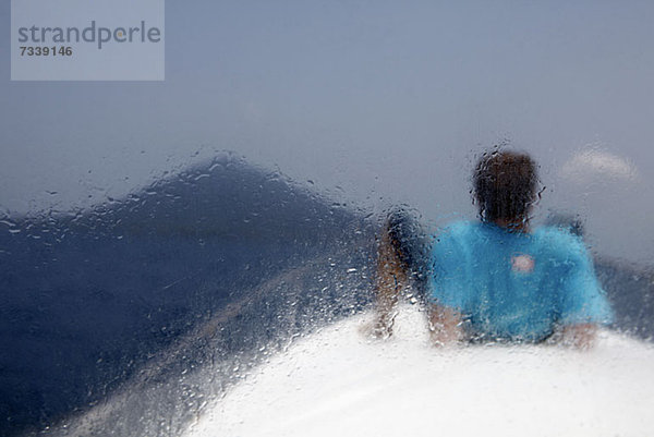 Ein auf einem Boot liegender Mann mit Blick auf den Vulkan Krakatau  Rückansicht  durchs Fenster gesehen