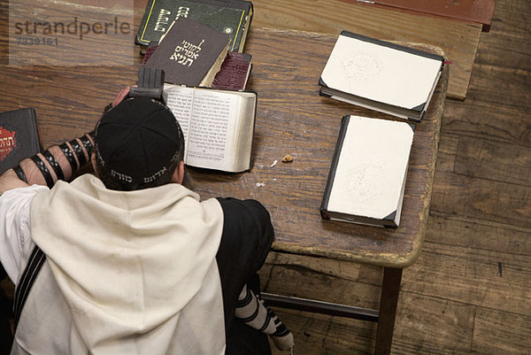 Jüdischer Mann mit Tefillin liest religiöses Gebetbuch