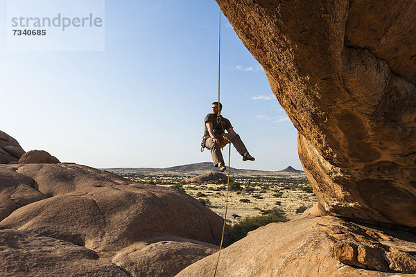 Junger Mann beim Abseilen vom Bogenfels  Spitzkoppe-Gebiet  Damaraland  Namibia  Afrika