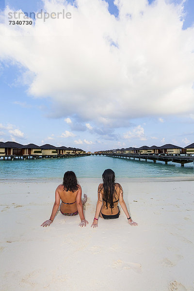 Zwei Mädchen  etwa 15 und 19 Jahre  sitzen am Strand an einer Lagune  hinten Paradise Island  Lankanfinolhu  Nord-Male-Atoll  Republik Malediven  Indischer Ozean  Asien
