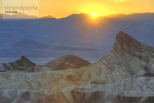Blick von Zabriskie Point  auch Zabriske Point  auf durch Mineralien verfärbtes erodiertes Gestein des Manly Beacon  Sonnenuntergang  dahinter Panamint Range  Sonnenuntergang  Death Valley Nationalpark  Mojave-Wüste  Kalifornien  Vereinigte Staaten von Amerika  USA