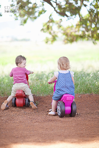 Kleinkinder reiten Spielzeug auf Schotterpiste