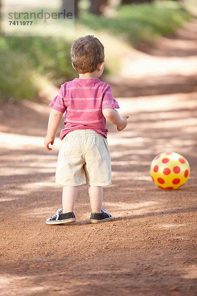 Kleinkind Junge mit Ball auf Schotterpiste