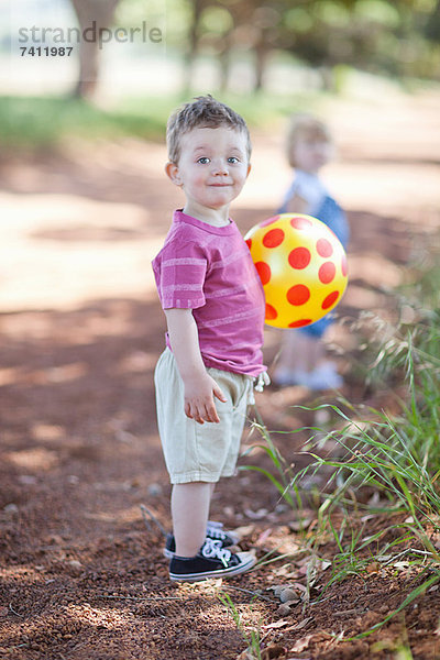 Kleinkind Junge mit Ball auf Schotterpiste