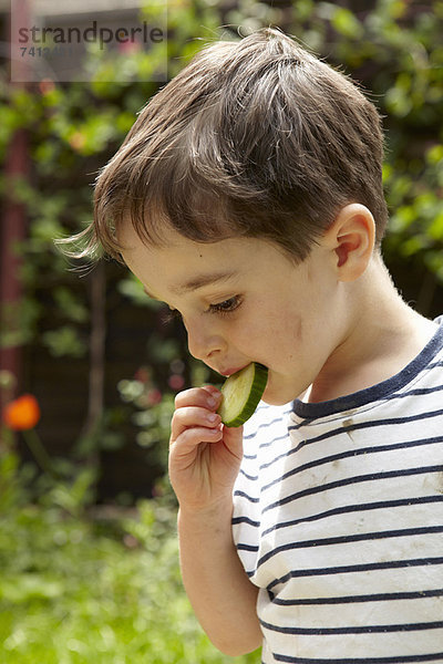 Junge isst Gurke im Freien