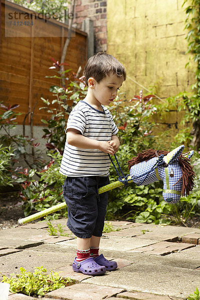 Junge spielt mit Spielzeugpferd im Garten