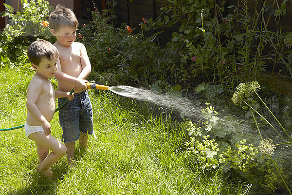 Jungen gießen Pflanzen im Garten