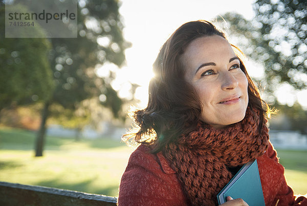 Lächelnde Frau hält Buch im Freien