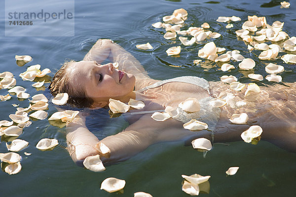 Frau schwimmt in Blütenblättern im stillen See