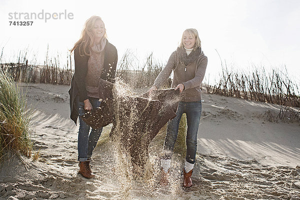 Frauen beim Ausschütteln der Stranddecke