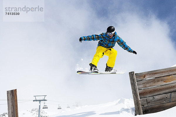 Snowboarder beim Springen vom Holzzaun