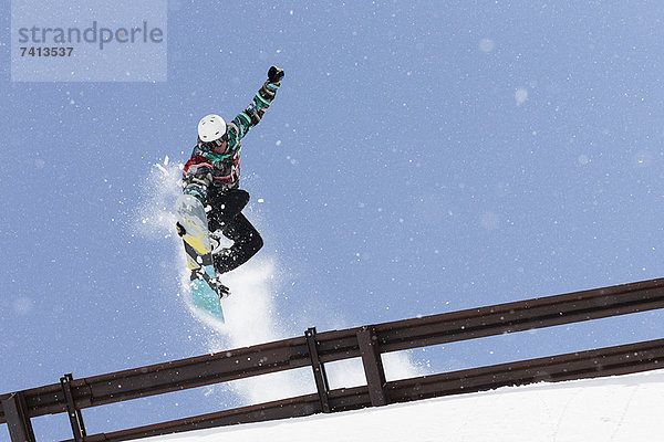 Snowboarder springt über Metallgeländer