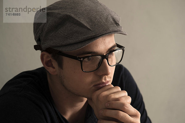 Nachdenklicher junger Mann mit Brille und Kappe