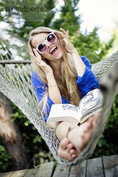 Farbaufnahme Farbe sitzend junge Frau junge Frauen lachen Buch Hängematte Kleidung Taschenbuch vorlesen
